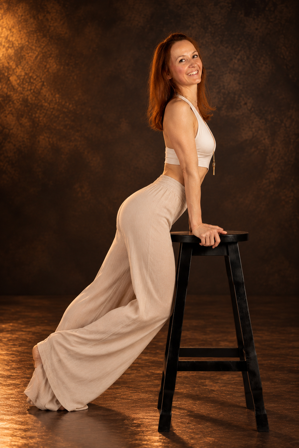 Leia P_Move with Leia 18 Leia, chair dance teacher, in beige wide-leg trousers and a white top posing next to a black stool